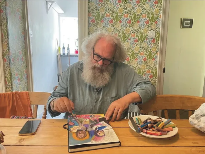 A man with a big white beard making a drawing at a table.