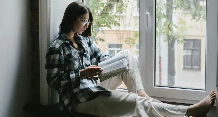 fair-skinned woman reading the bible in the windowsill