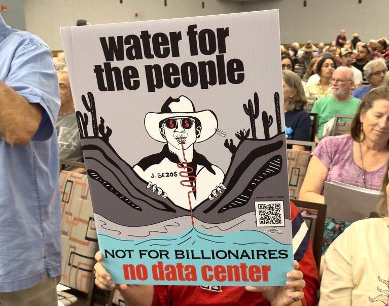 People at a community meeting in the U.S. to discuss a massive data center installation, in the foreground is a sign against the data center.