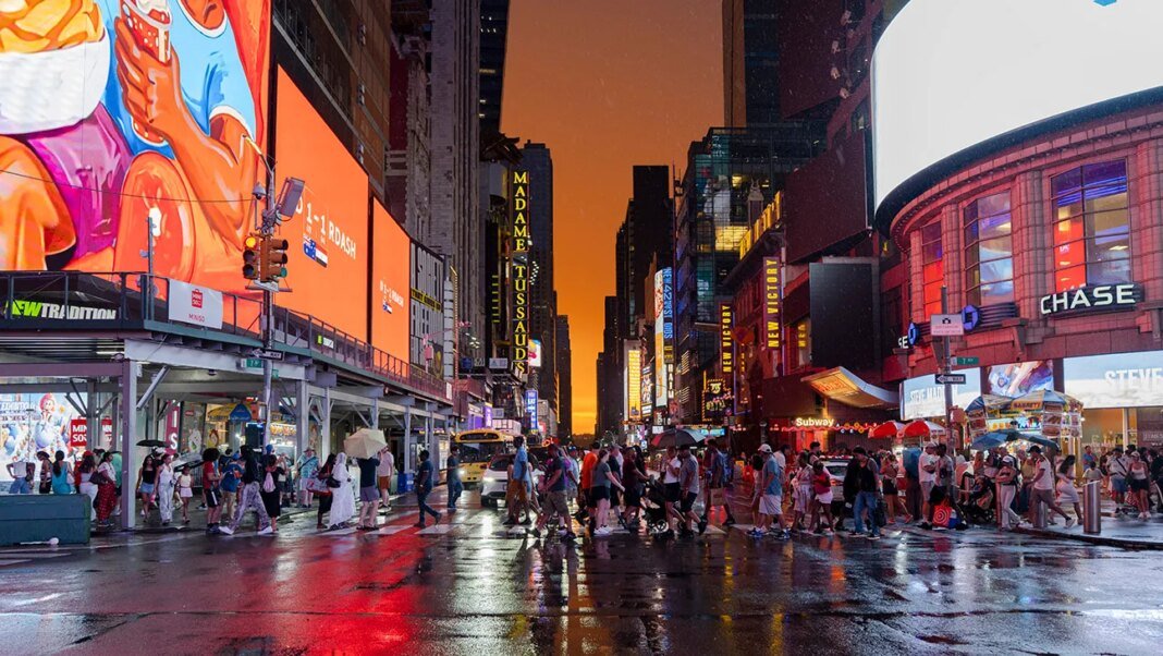 People cross 7th Avenue during a colorful sunset in Times Square after a rain shower on July 03, 2026 in New York, New York. The heat wave, stretching from the midwest to east coast, will affect as many as 90 million Americans.