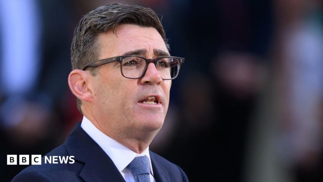 A close up shot shows Andy Burnham speaking outside Downing Street, wearing glasses and a dark suit and tie, with a bokeh background.