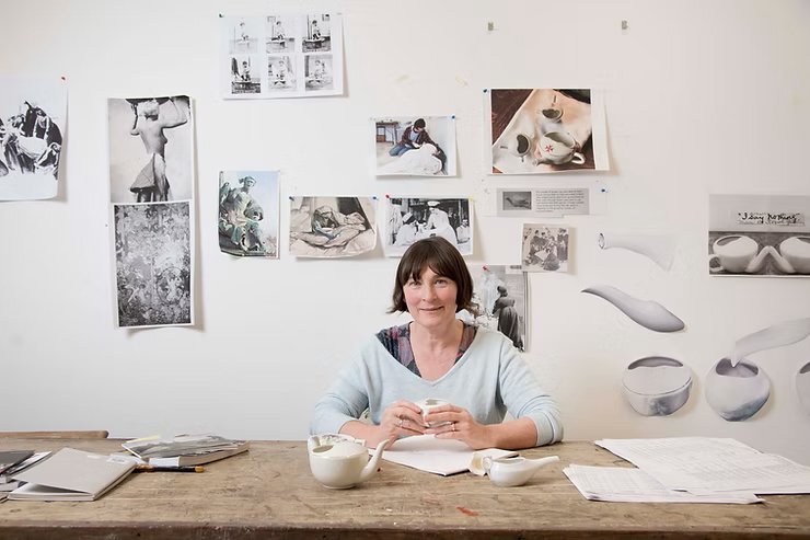 Christine Borland, Artist Who Researched Histories of Science and Medicine, A woman sitting at desk with ceramic pots and research documents behind her.