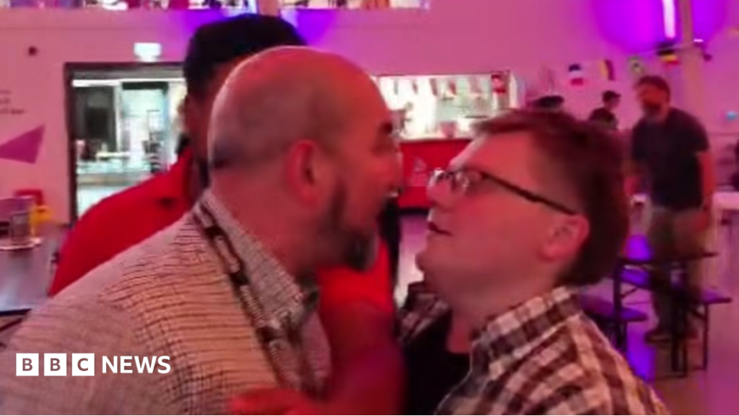 Inquiry into Farage poster row at anti-racism show A man with a bald head wearing a checked shirt has an argument with a person in a checked shirt, glasses and short brown hair