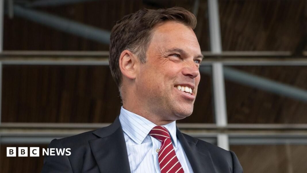 Ken Skates smiling off to the side of the image, wearing a dark suit and red and white tie, with a pin stripe shirt.