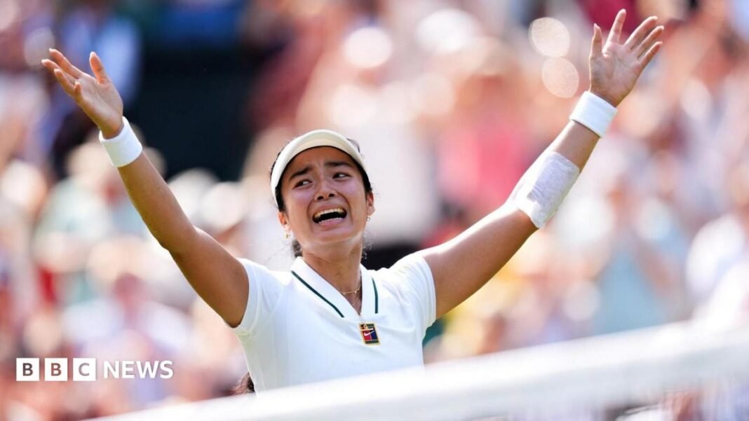Filipina tennis player Alexandra Eala raises his arms after a Wimbledon match, net in front of her and a blurred image of the crowd in the background.