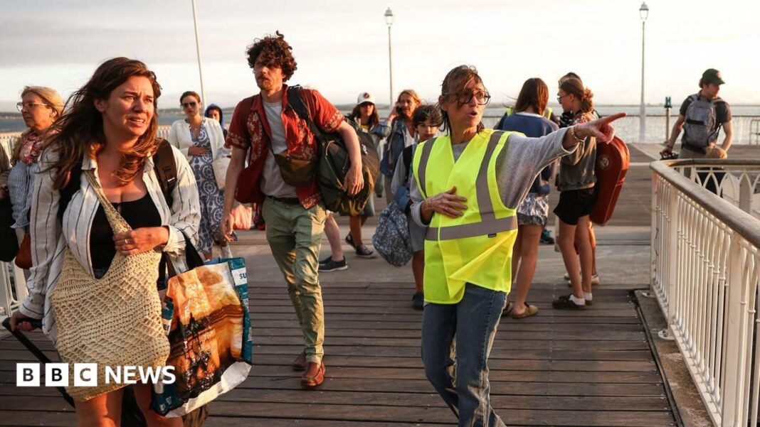 A volunteer gives indication to holidaymakers from Lege-Cap-Ferret upon their arrival in Arcachon by boat during an evacuation operation of the entire Cap-Ferret peninsula, in southwestern France, on July 24, 2026 whilst a wildfire is spreading across the area