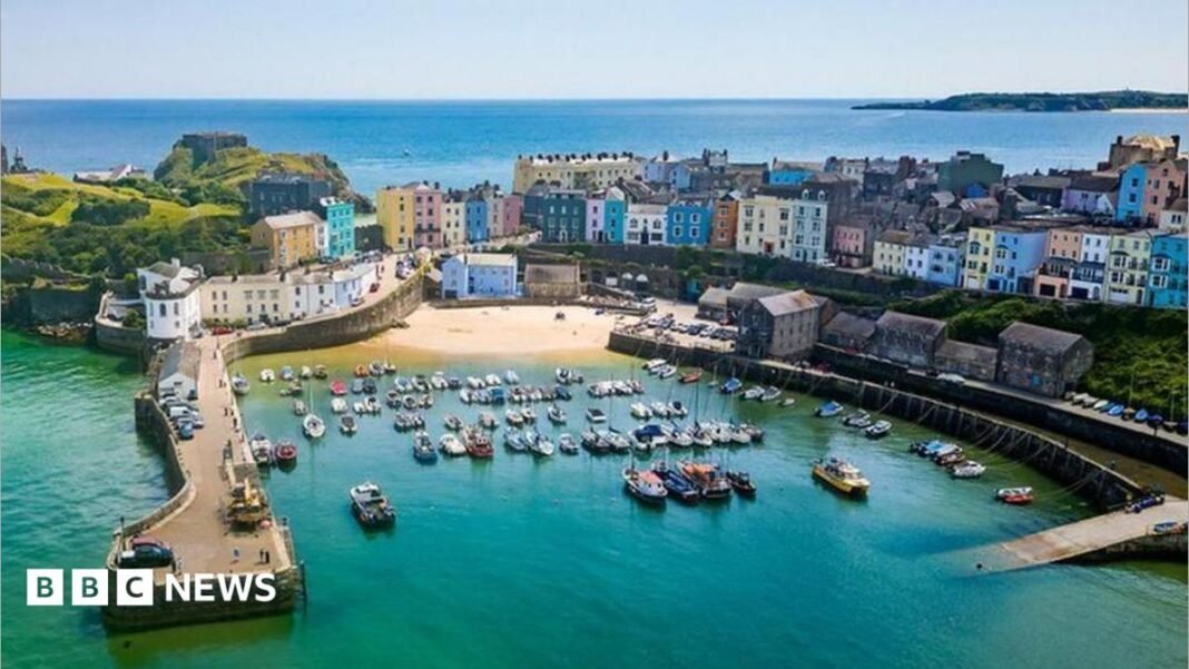 An aerial shot of Tenby harbour in Pembrokeshire, showing docked boats and colourful houses on the seafront.