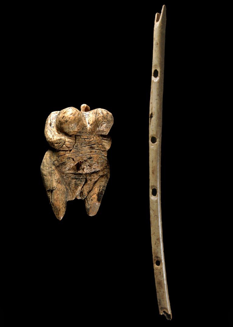 A composite image of a small carved female figurine t and a slender bone flute with finger holes on the right, on a black background