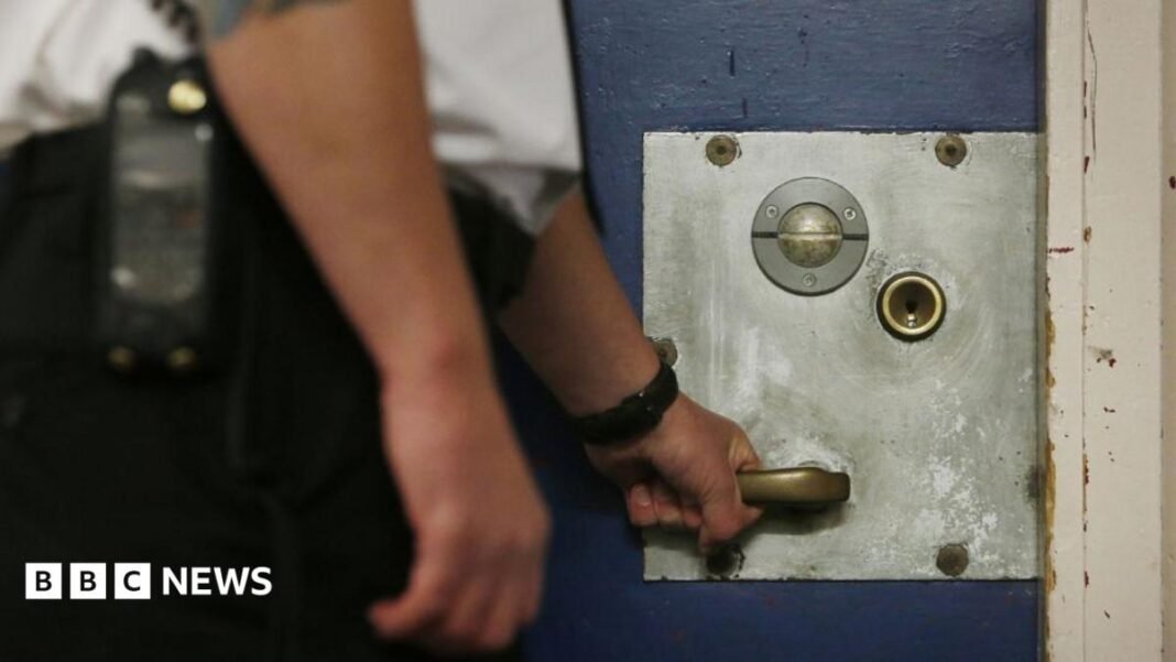 A prison officer with his left hand on a cell door. His upper and lower body is out of shot. 
